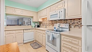 A kitchen with light-colored cabinets, a microwave, an oven, a dishwasher, and a tiled backsplash.
