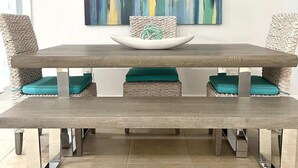 Een eethoek met een houten tafel, kussens in teal en een geweven hanglamp.