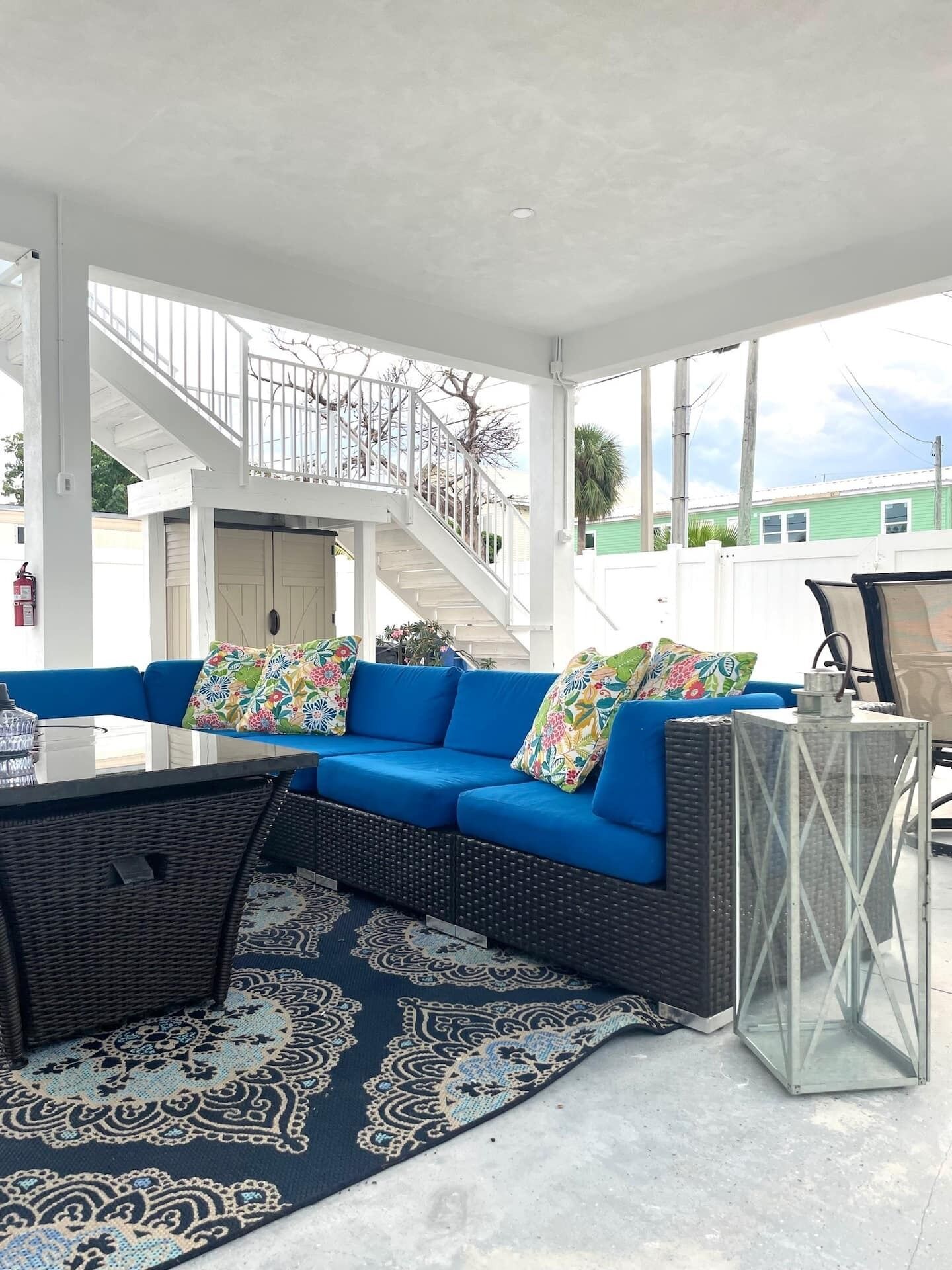 A covered outdoor seating area with a blue sofa, patterned rug, and a lantern.