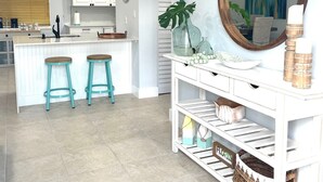 Een moderne keuken met witte kastjes, een centraal eiland met krukken, een grote spiegel en een decoratieve plant.