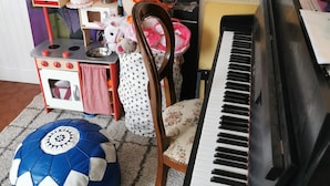 A room with a piano, a soccer ball, a chair, a small table with a cake, and a painting on the wall.