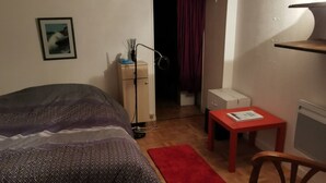 A bedroom with a bed, a desk, a chair, a red rug, and a small table.
