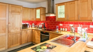 A modern kitchen with wooden cabinets, a red tiled backsplash, stainless steel appliances, and a central island with a sink. - Littleham Court Cottage (Bideford)