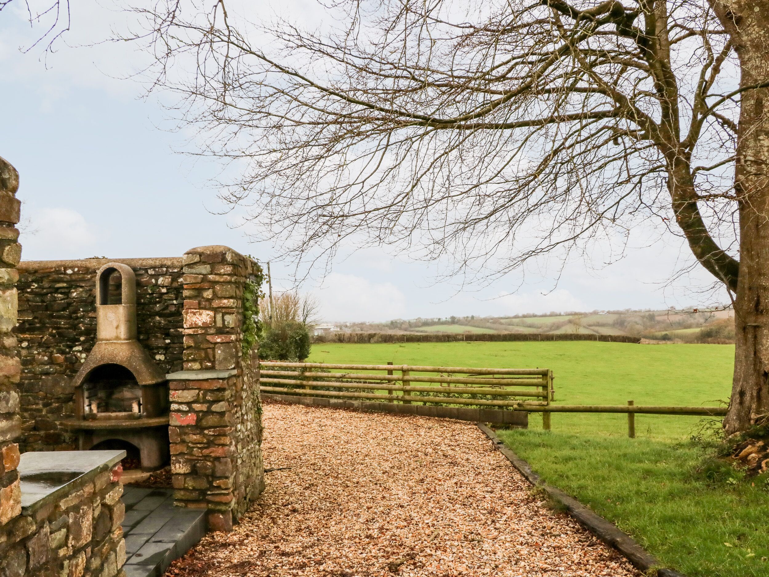 A rustic stone building with a chimney, a gravel path, and a wooden fence in a rural setting.