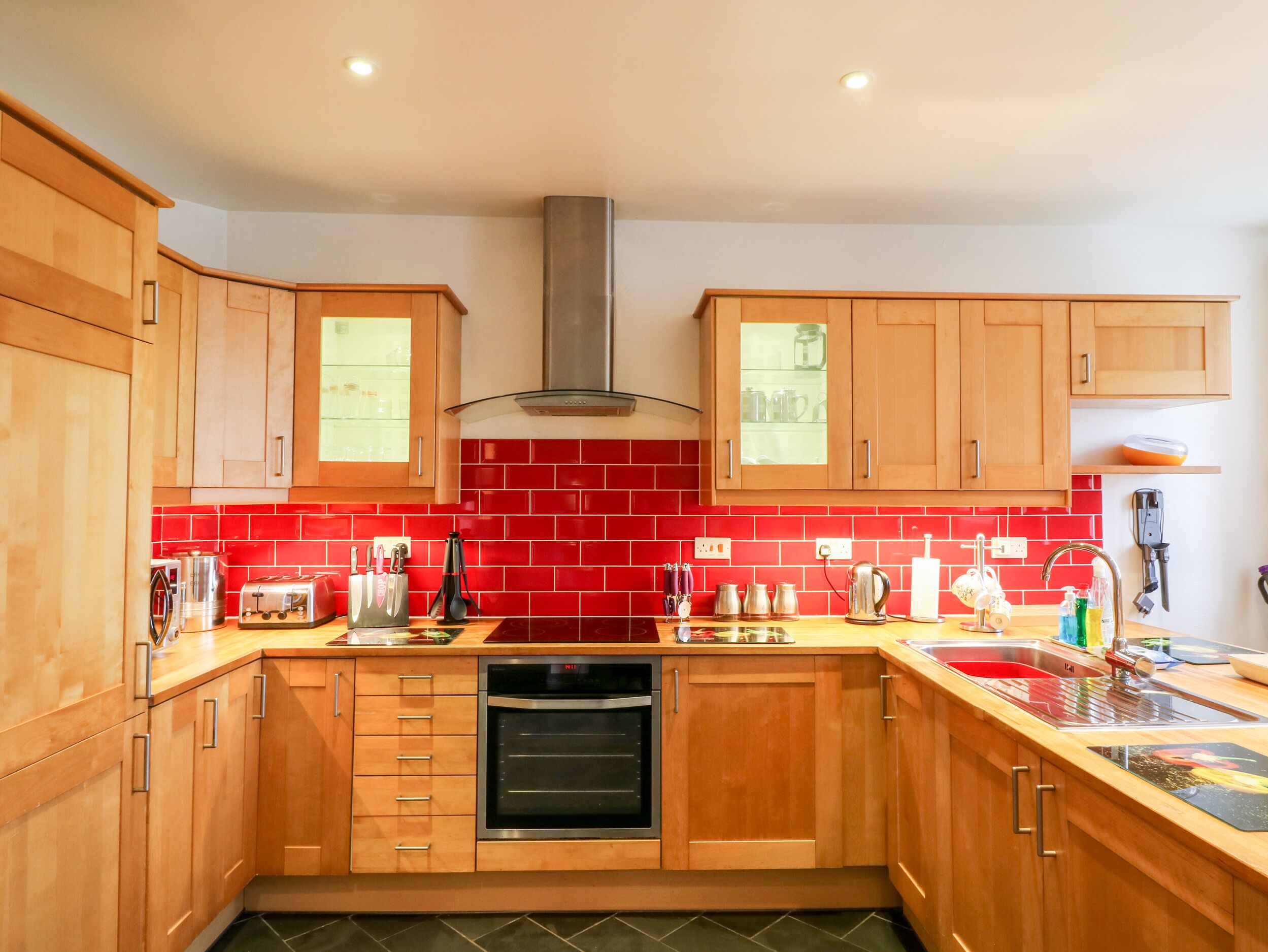Una cucina moderna con mobili in legno, forno in acciaio inossidabile e zoccolo di piastrelle rosse.