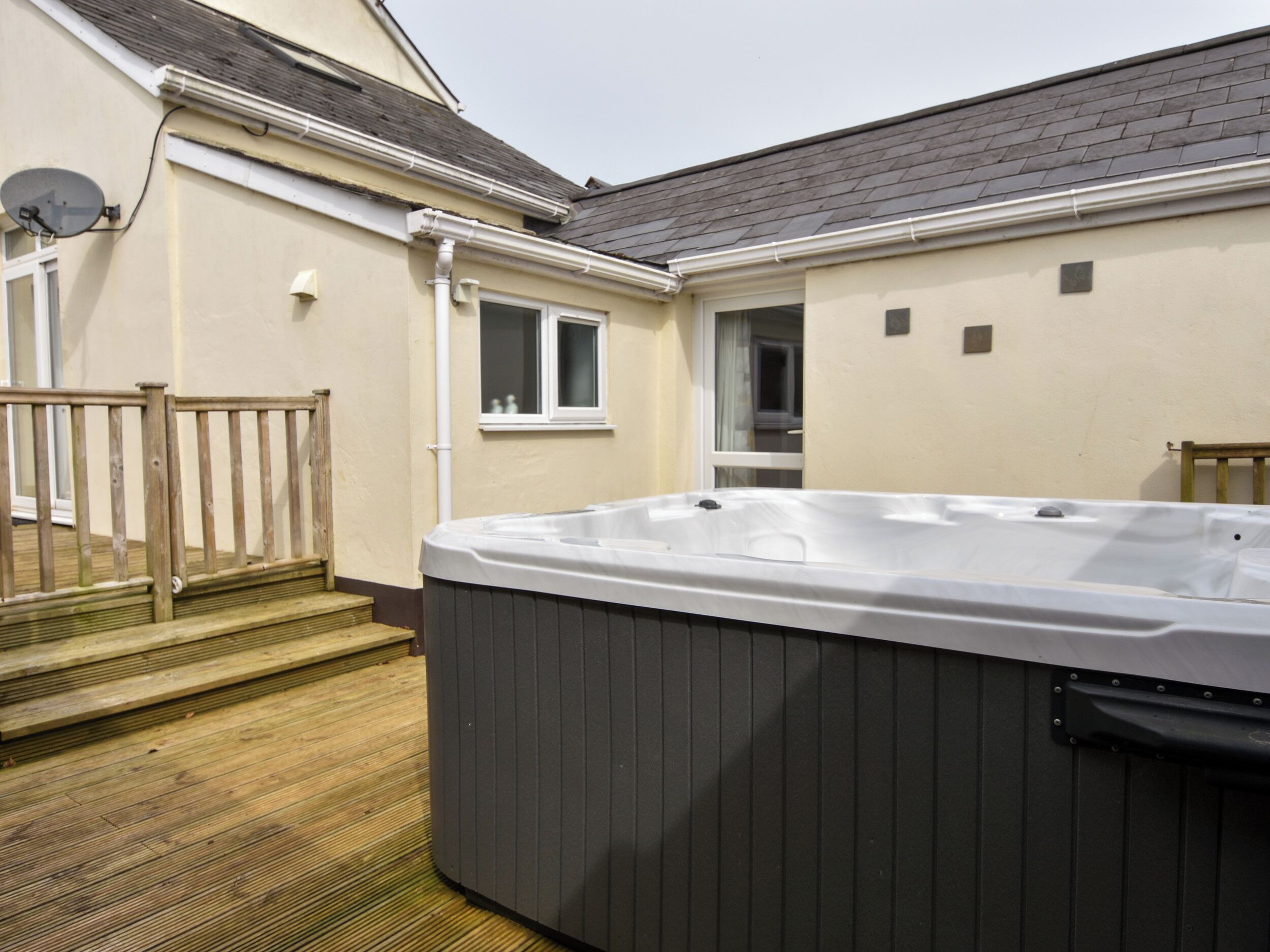 Un bain à remous installé dans un jardin, avec une terrasse en bois, une fenêtre et une porte donnant sur un espace abrité.
