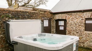 A hot tub in a rustic outdoor setting with stone walls and wooden benches. - Littleham Court Cottage (Bideford)