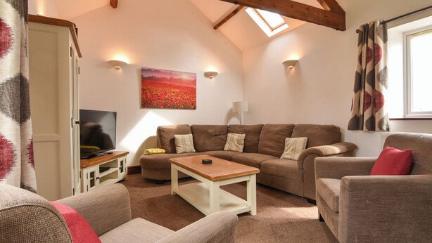 A cozy living room with a high ceiling, a sofa set, a coffee table, and a flat-screen TV. - Littleham Court Cottage (Bideford)