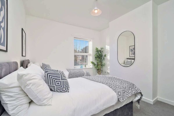 Relax in this serene bedroom with a large bed, flanked by a window and a mirror.