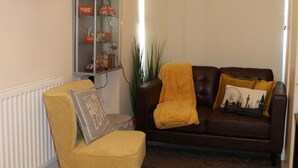 A living room with a yellow armchair, a brown leather sofa with yellow cushions, and a glass cabinet with decorative items.