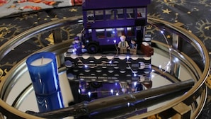 A purple double-decker bus model on a reflective surface with a blue candle and a book titled "F. Scott Fitzgerald is the Night".