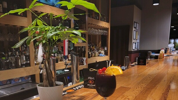 A restaurant setting with a bar area, a television displaying a sports game, a potted plant, a glass of red wine, and a plate of soup. - Masters rental - Historic federal in the heart of Edgefield county (Johnston)