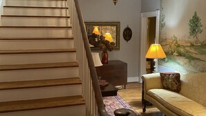 A staircase with wooden steps and a metal handrail, a chandelier, a sofa, a patterned rug, and a wall with a painting. - Masters rental - Historic federal in the heart of Edgefield county (Johnston)