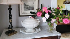 A marble table with a white tureen, a black lamp, and a vase of pink flowers. There are two framed black-and-white photographs on the wall. - Masters rental - Historic federal in the heart of Edgefield county (Johnston)