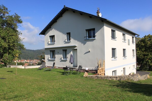Ein zweistöckiges Gebäude mit flachem Dach, mehreren Fenstern und einer kleinen Terrasse mit Gartenmöbeln.