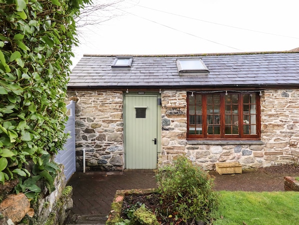 A stone building with a green door, a sign reading "Little Orchard," and a window with multiple panes.