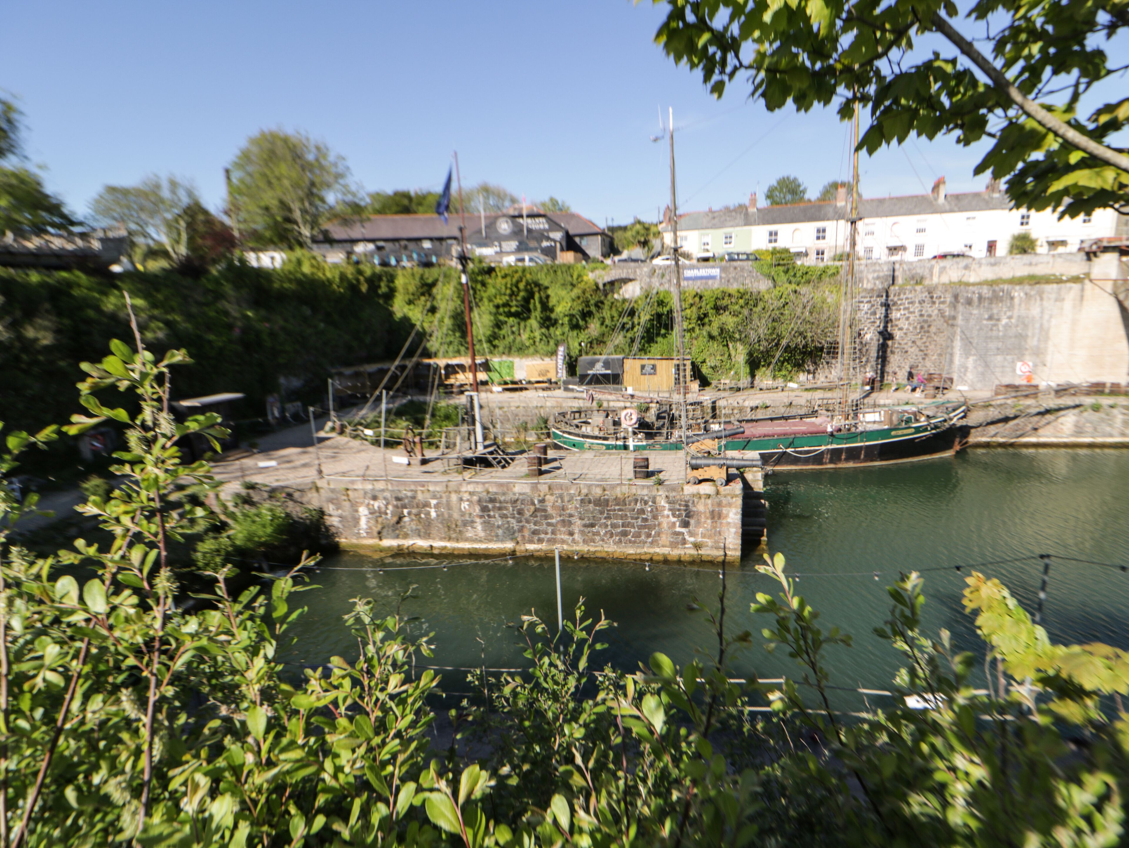 A harbor with boats docked, a stone pier, and buildings in the background.