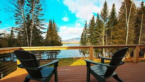 A deck with two Adirondack chairs overlooking a lake, surrounded by trees and a clear sky. - Dodge Lodge | Private Waterfront on Dodge Pond, Newly Renovated, Near Downtown Rangeley (Rangeley)