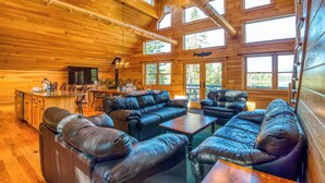 A log cabin interior with a large leather sofa, wooden dining table, and a kitchen area with a bar. - Dodge Lodge | Private Waterfront on Dodge Pond, Newly Renovated, Near Downtown Rangeley (Rangeley)