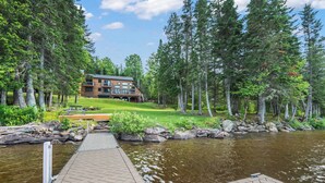 A lodge with a dock extending into a calm river, surrounded by dense forest. - Dodge Lodge | Private Waterfront on Dodge Pond, Newly Renovated, Near Downtown Rangeley (Rangeley)