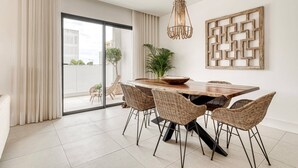 A modern dining area with a wooden table, wicker chairs, a hanging light fixture, and a geometric wall art piece.