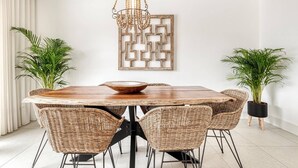 A dining area with a wooden table, wicker chairs, and potted plants.