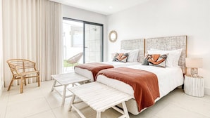 A modern hotel room with a large bed, two bedside tables, a chair, and a view through a sliding glass door.
