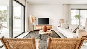 A modern living room with a large TV, a sofa, and wicker chairs.