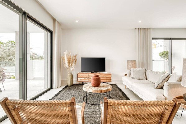 A modern living room with a large TV, a sofa, and wicker chairs.