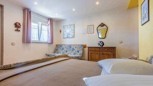 Une chambre à coucher avec un lit, une chaise, une commode et une fenêtre avec des rideaux.