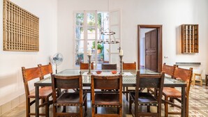 A dining area with a glass table surrounded by wooden chairs, a hanging light fixture, and a view of the outdoors through a large window. - Casa Metge Vidal by Balearic Villas (Pollensa)