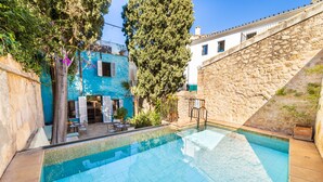 A swimming pool with tiled edges, surrounded by a stone wall and a building with a blue facade. - Casa Metge Vidal by Balearic Villas (Pollensa)
