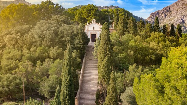 A building with a central entrance, surrounded by dense trees and hills in the background. - Casa Metge Vidal by Balearic Villas (Pollensa)