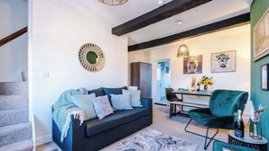 Una sala de estar moderna con un sofá azul oscuro, un sillón verde y una alfombra de mármol. Hay un comedor con mesa y sillas, y una escalera a la izquierda.