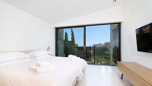 A modern bedroom with a large bed, a TV mounted on the wall, and a balcony with a mountain view. - Casa Liebre by Balearic Villas (Pollensa)