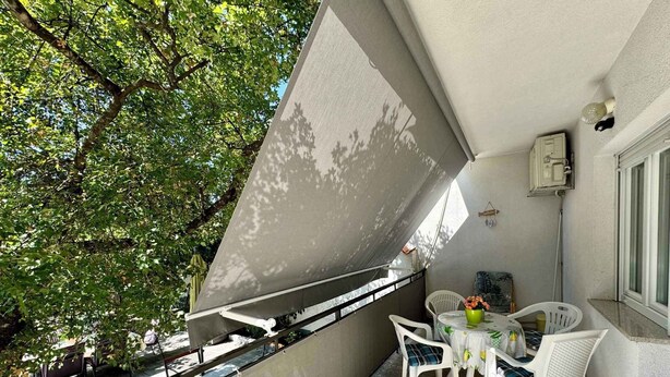 Een balkon met een tafel en stoelen, een plant in een pot en uitzicht op bomen.