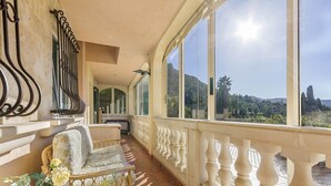 A balcony with a view of a mountainous landscape, a wicker chair, and a potted plant.