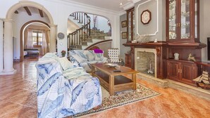 A spacious living room with a large sofa, a coffee table, and a fireplace. There is a staircase leading to another level.