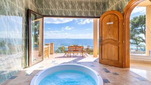 Una bañera de hidromasaje con vista al mar, una puerta de madera y una puerta de cristal que da a un área de estar al aire libre.