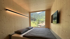 Een slaapkamer met een bed, een raam met uitzicht op een groen landschap en een televisie aan de muur.