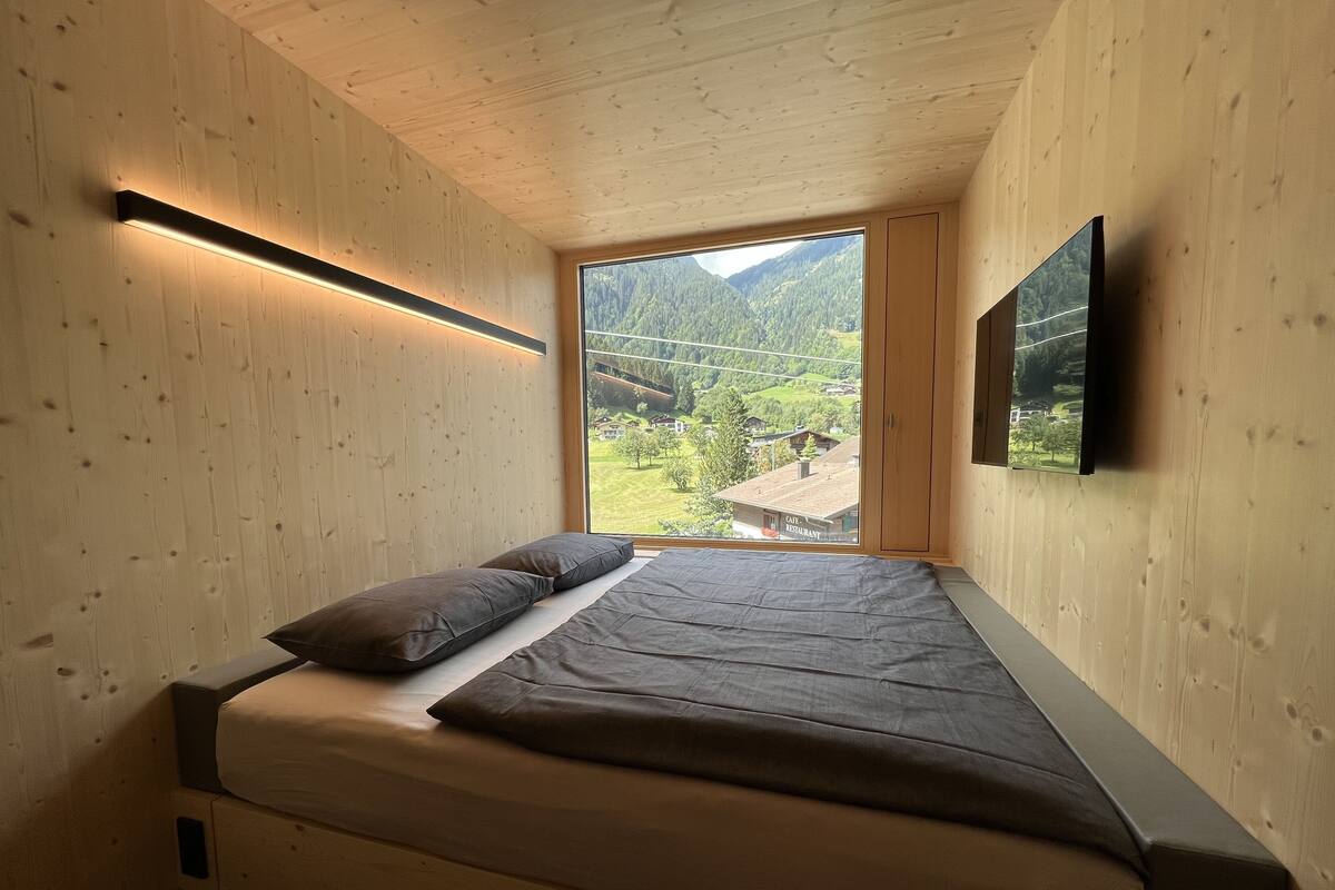 Une chambre à coucher avec un lit, une fenêtre donnant sur un paysage verdoyant et un téléviseur fixé au mur.