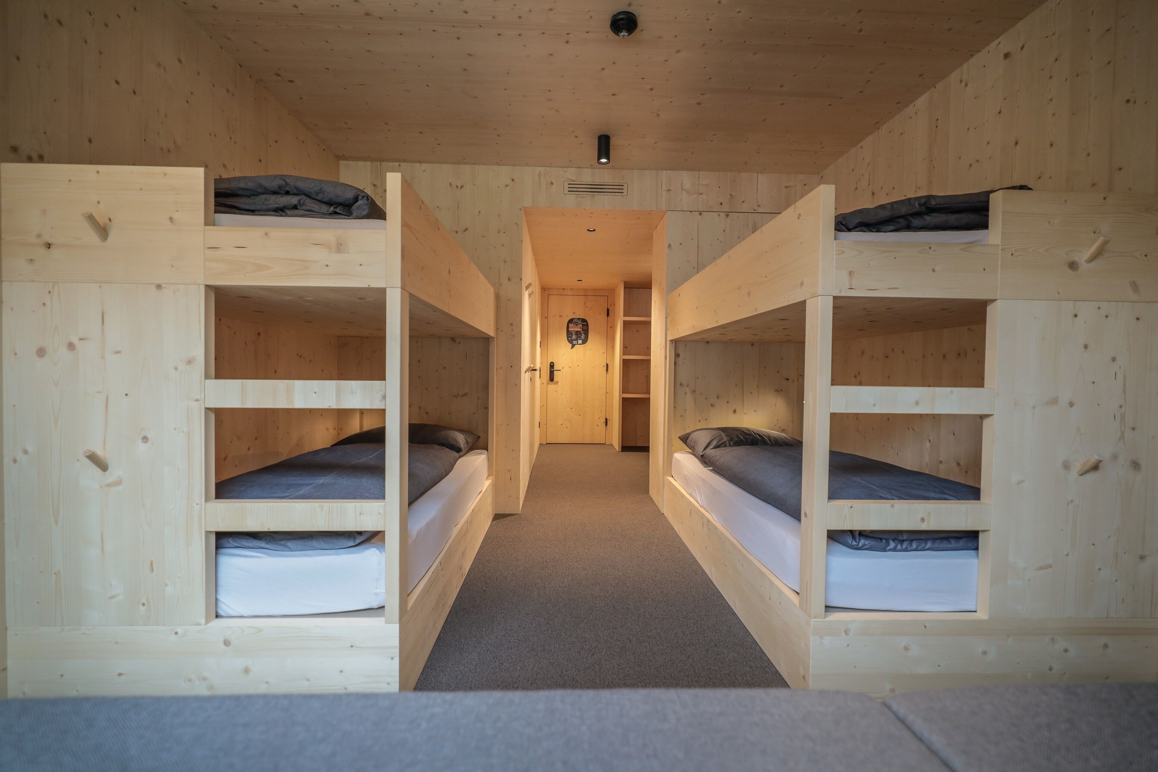 A wooden bunk bed room with a carpeted floor and a door at the end of the hallway.