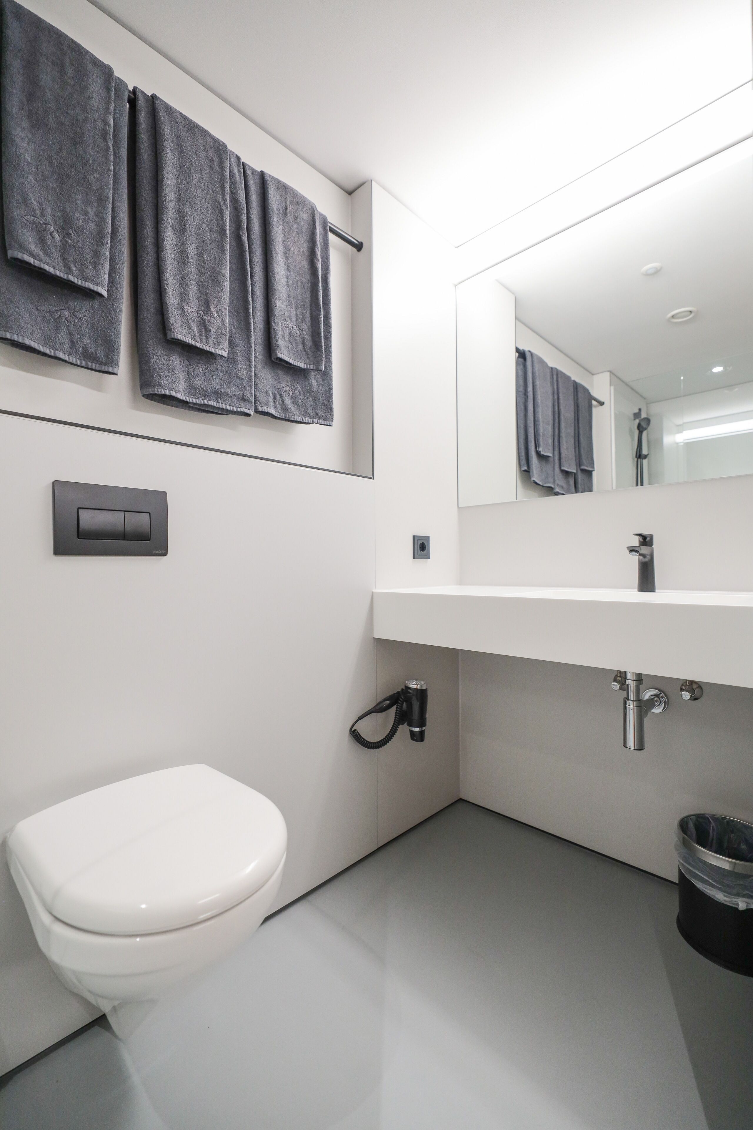 Ein modernes Badezimmer mit Toilette, Waschbecken mit Spiegel darüber und Handtuchhalter mit dunklen Handtüchern.