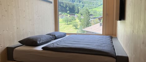 A bedroom with a bed, a window, and a view of a green landscape.
