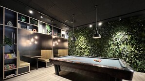 Een pooltafel in een ruimte met een houten vloer, boekenplanken en een wand begroeid met groene bladeren.