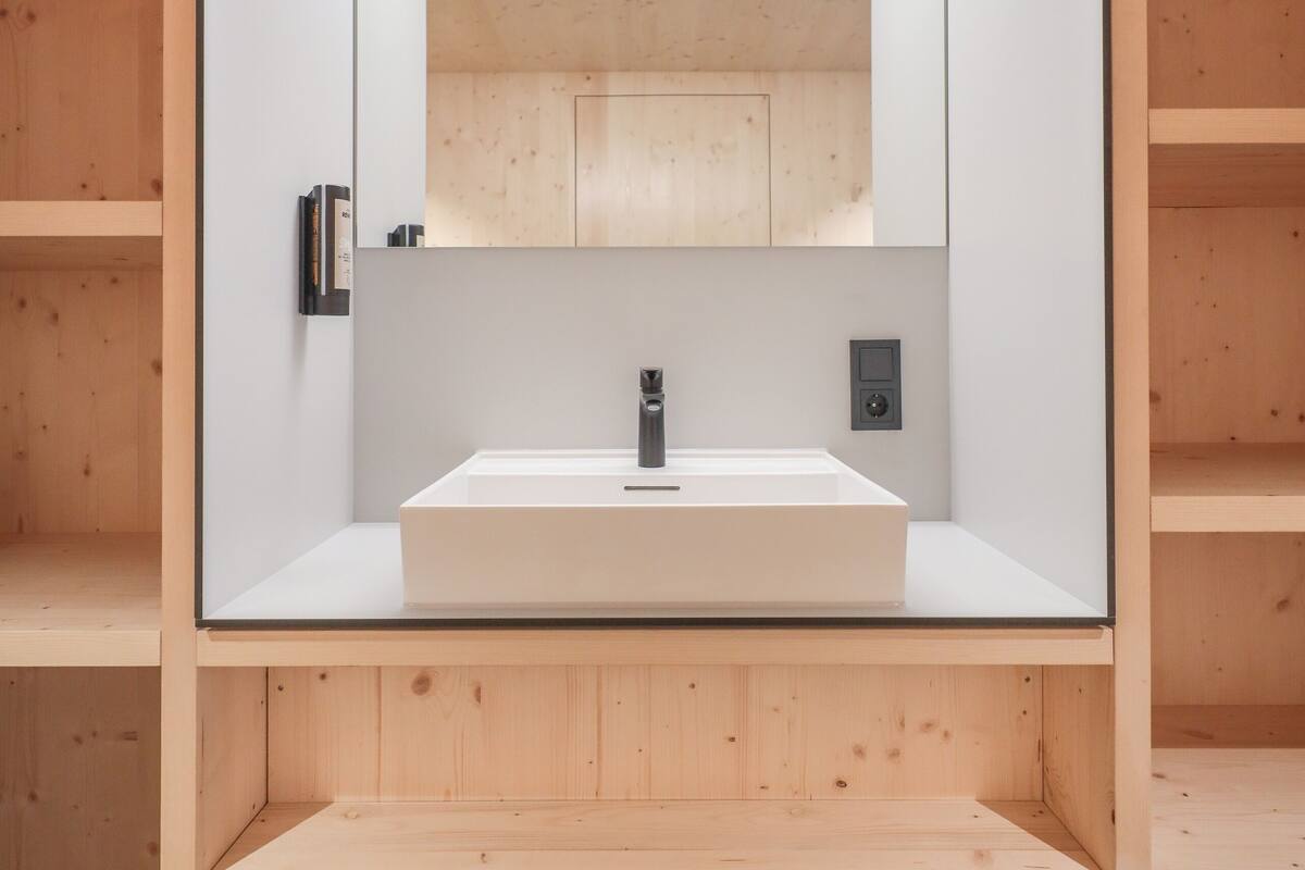 Une salle de bain moderne avec un lavabo central, un grand miroir et un lambris en bois sur les murs.