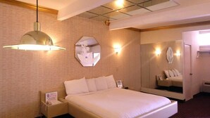 A hotel room with a large bed, a bedside table, a mirror, and a shower area. - Commack Inn (Commack)