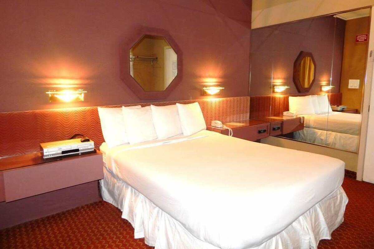 A hotel room with a large bed, bedside tables, a mirror, and wall-mounted lights.