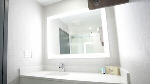 A modern bathroom with a large mirror, a sink, and a toilet paper holder. - Commack Inn (Commack)