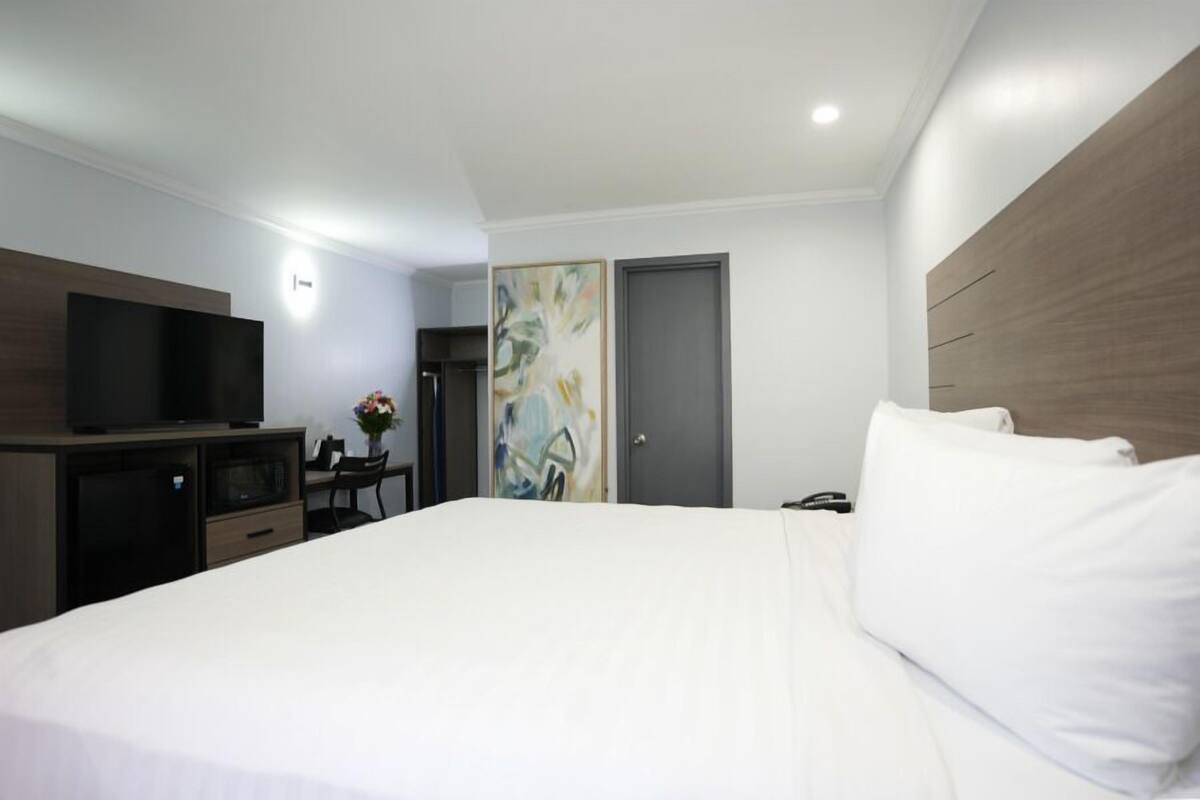 A hotel room with a large bed, a desk with a chair, a television, and a door with a painting.